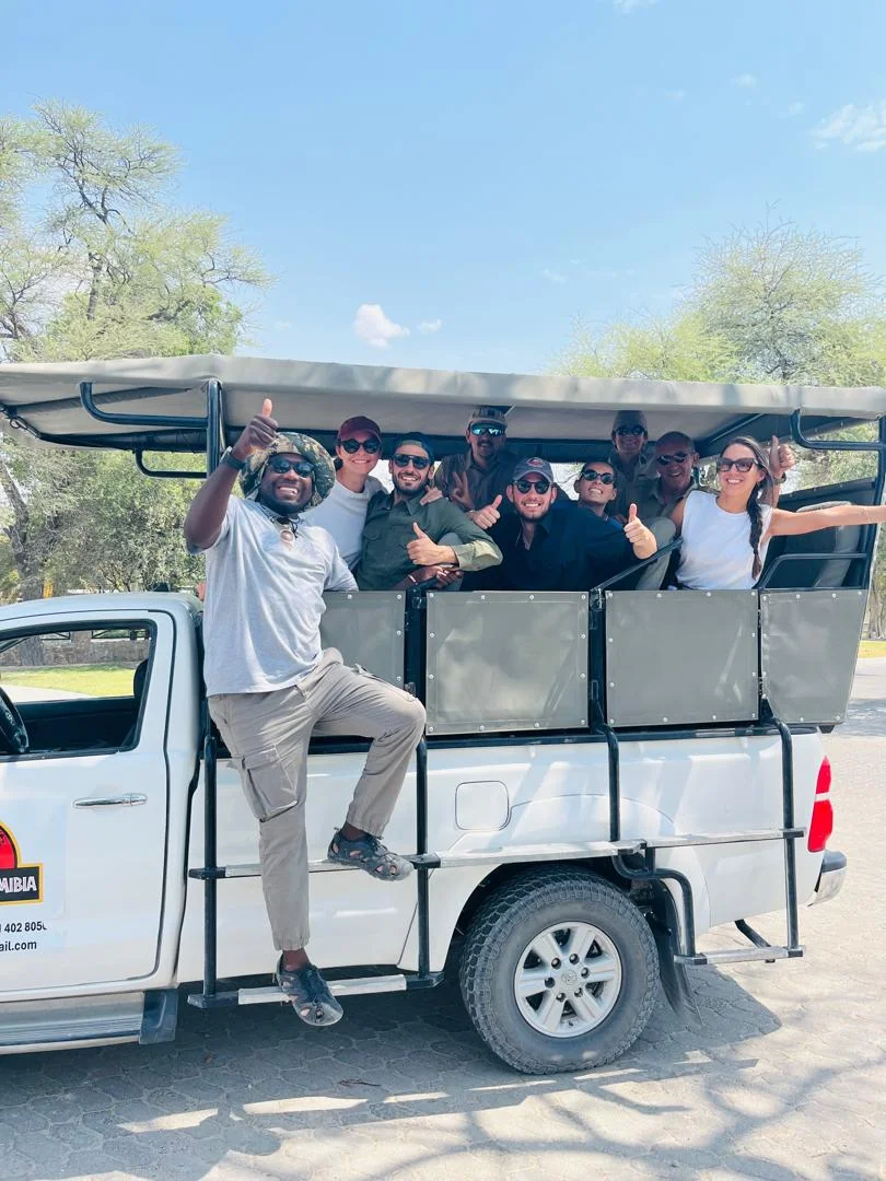 Gruppo felice di turisti che alza il pollice sul veicolo safari Tom Safari Namibia, Etosha