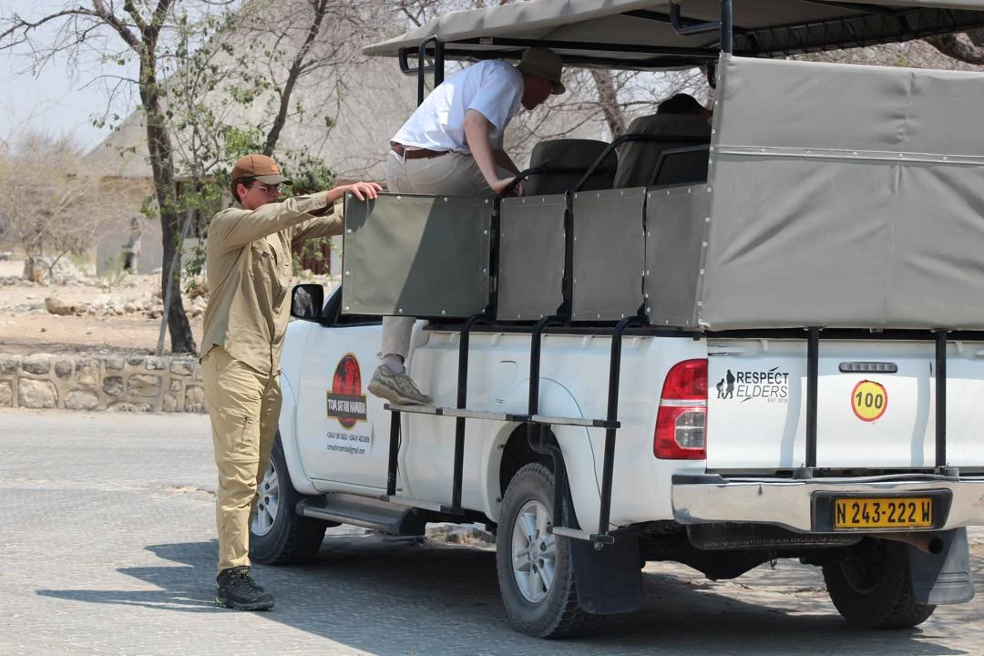 Guida safari che aiuta un turista a salire sul veicolo safari Tom Safari Namibia